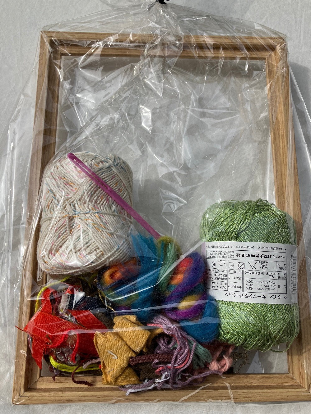 Plastic wrapped weaving kit with colorful yarn, pink plastic needle, and wooden frame