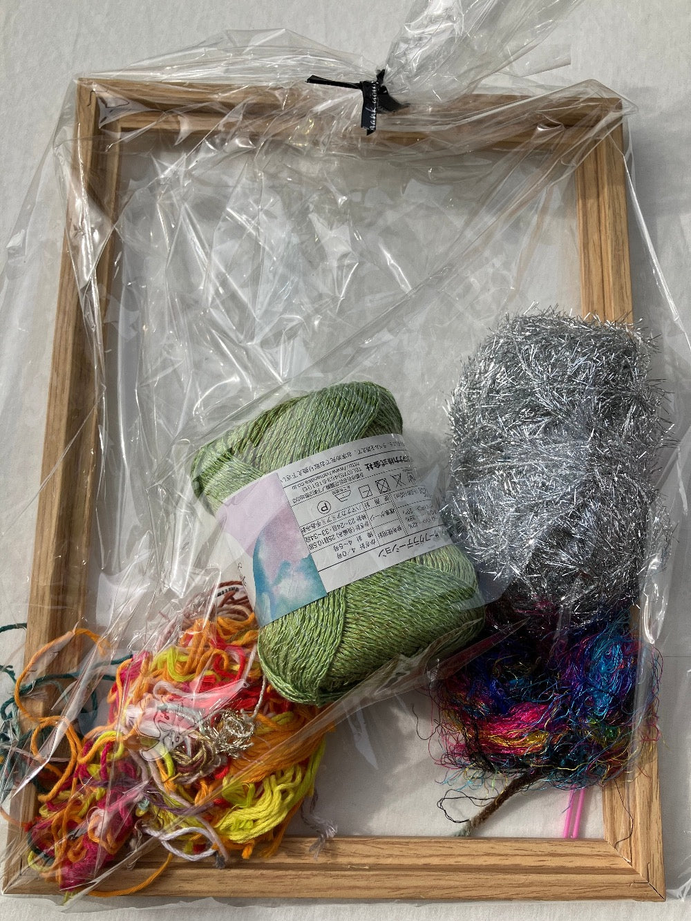 Plastic wrapped weaving kit with colorful yarn, pink plastic needle, and wooden frame