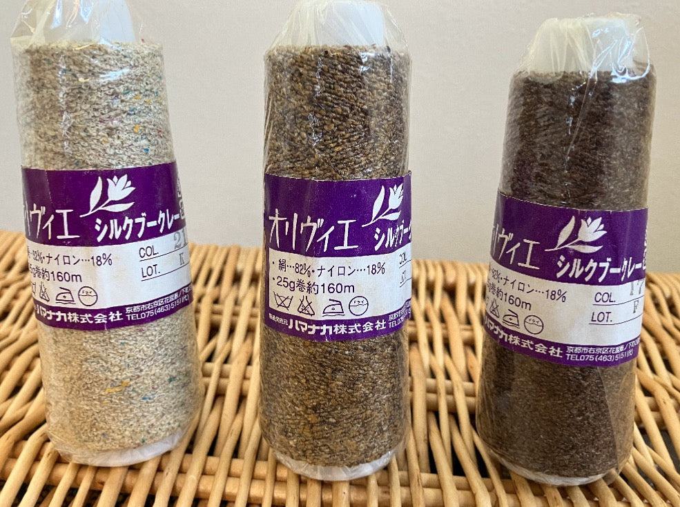Three cones of brown shade boucle yarn in plastic wrap with Japanese lettering