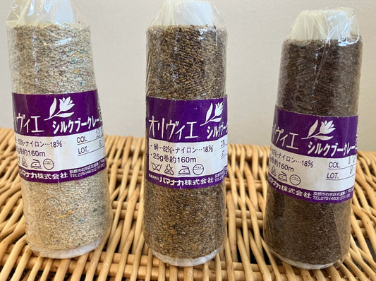Three cones of brown shade boucle yarn in plastic wrap with Japanese lettering