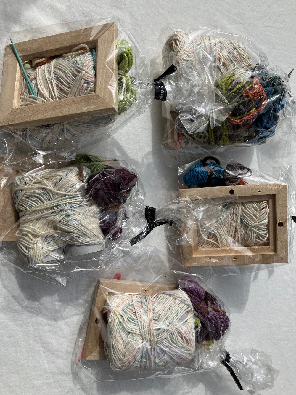 Five plastic wrapped weaving kits with colorful yarn, blue plastic needle, and wooden frames
