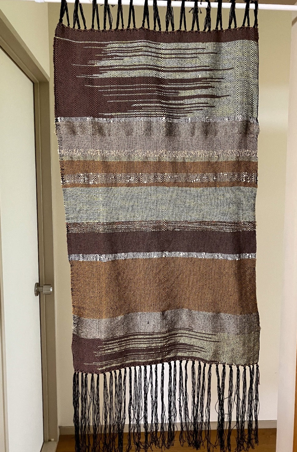 Brown and tan lines and zigzags panel curtain with black fringes hangs in interior doorway