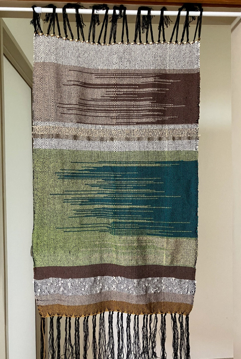 Brown, green, and tan lines and zigzags panel curtain with black fringes hangs in interior doorway