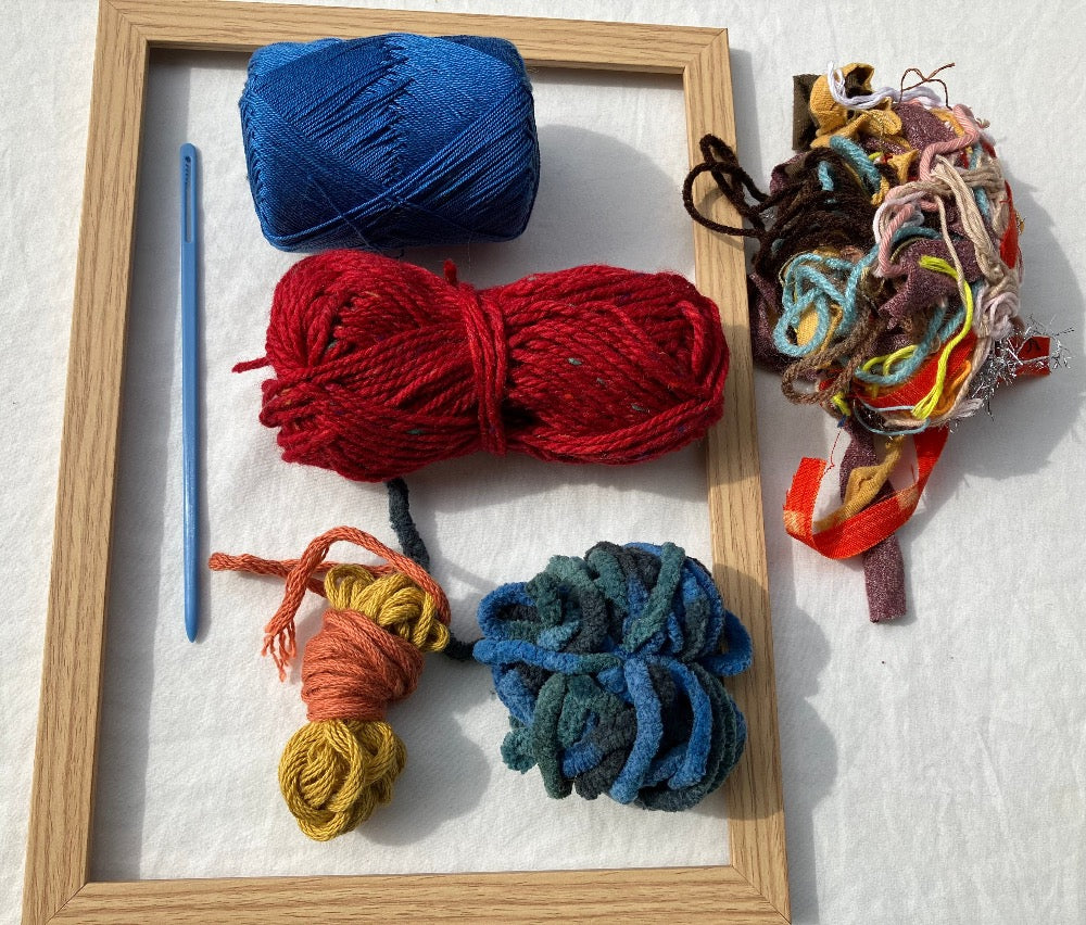 Unwrapped weaving kit with colorful yarn, blue plastic needle, and wooden frame