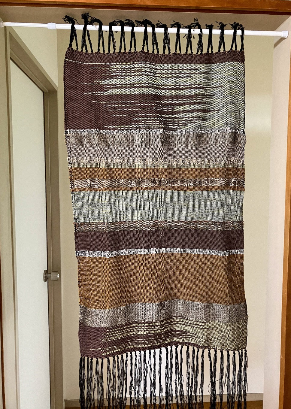 Brown and tan lines and zigzags panel curtain with black fringes hangs in interior doorway