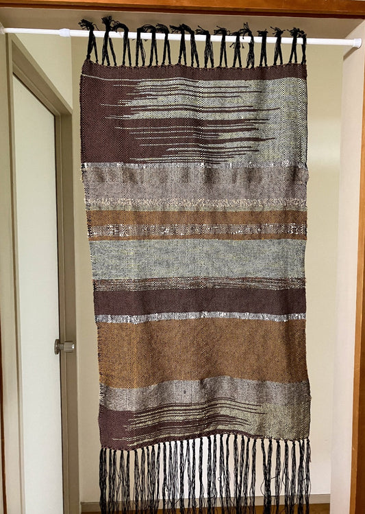 Brown and tan lines and zigzags panel curtain with black fringes hangs in interior doorway