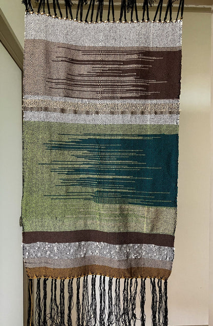 Brown, green, and tan lines and zigzags panel curtain with black fringes hangs in interior doorway