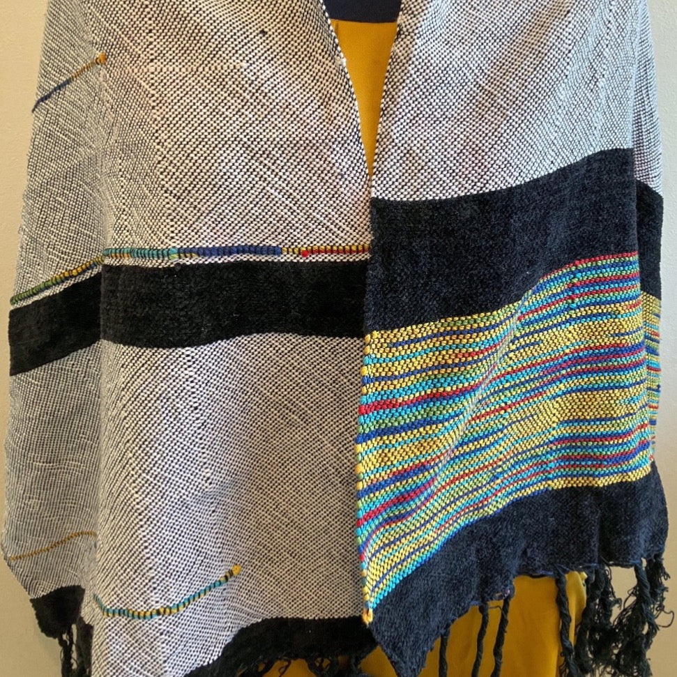 Female mannequin wearing black and white shawl with multicolor accents and side. There are two blocks of velvety black yarn accents.